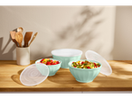 Three mint mixing bowls with lids, filled with salads, on a wooden table.