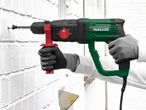 Person drilling into a white brick wall with a green and black rotary hammer drill.