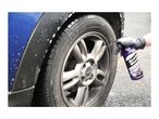 A person in a black glove sprays wheel cleaner onto a dirty car wheel.