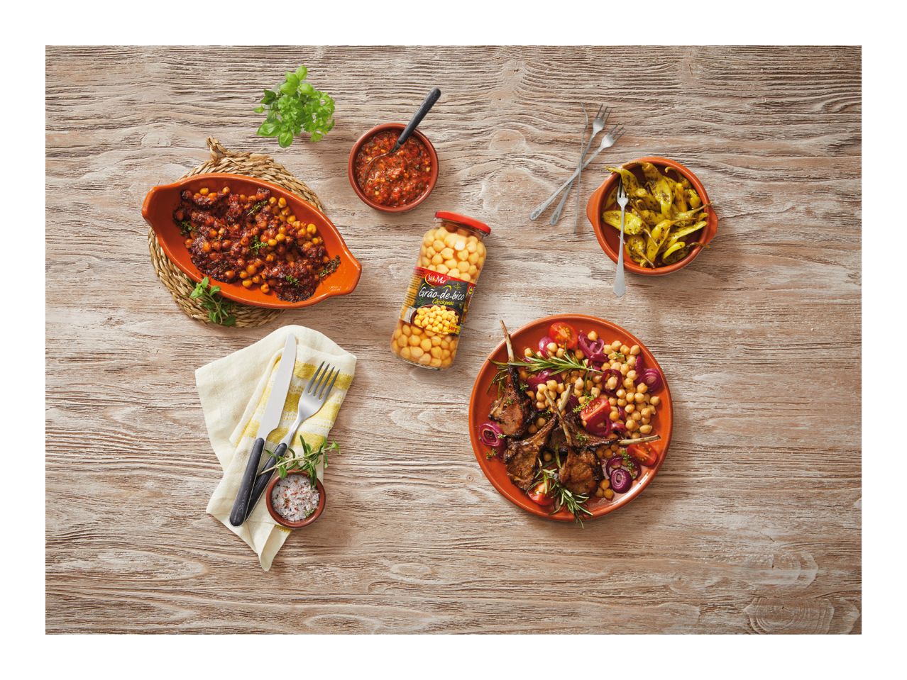 Overhead shot of a meal with lamb chops, chickpeas, tomatoes, onions, and various side dishes.