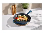 Cast iron pan with salmon and vegetables, next to salt and pepper mills and a potted herb.