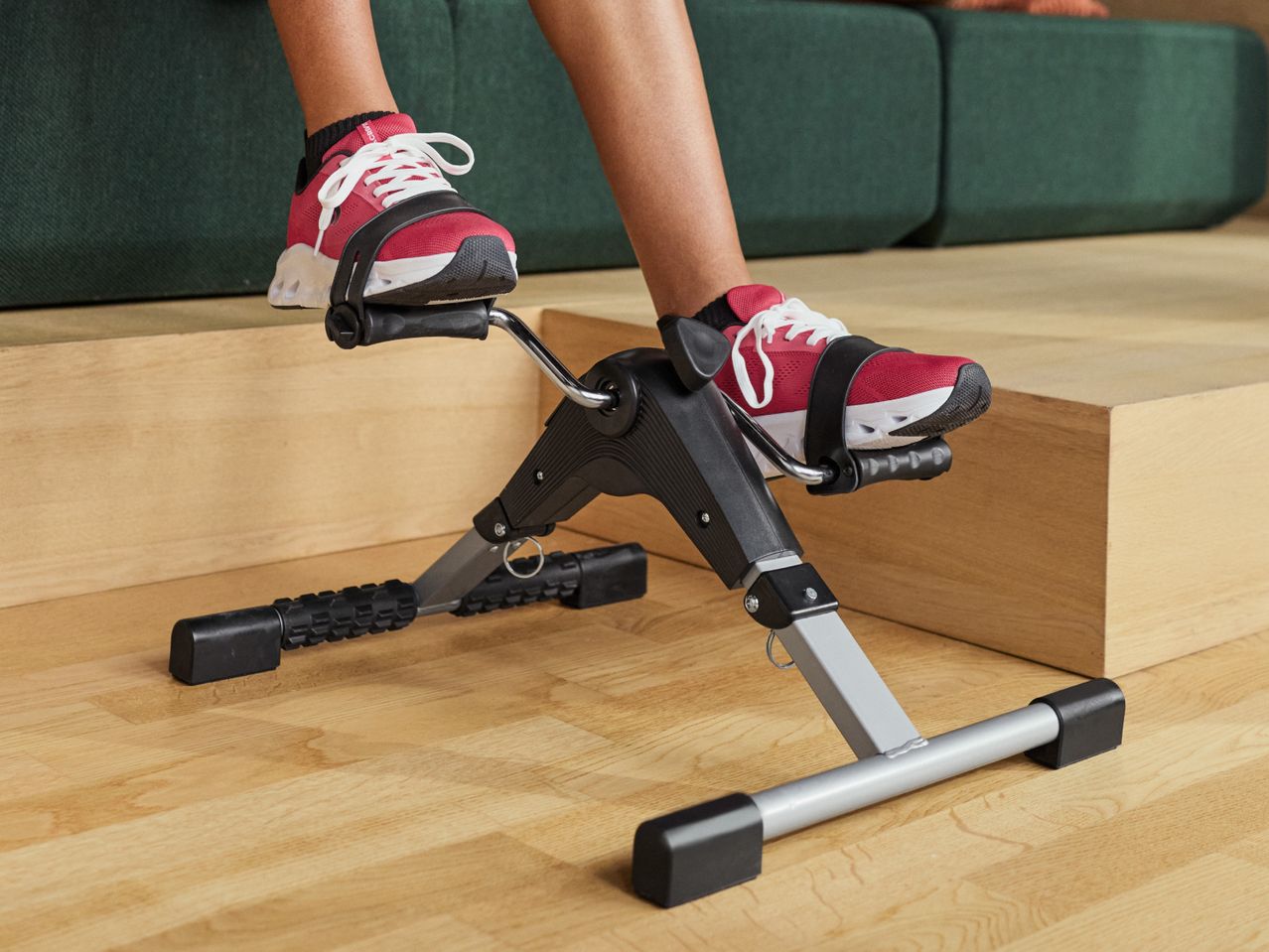 Person exercising with a mini exercise bike, wearing red and white sneakers.