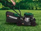 Person operating a petrol lawnmower with a black grass collection bag on green grass.