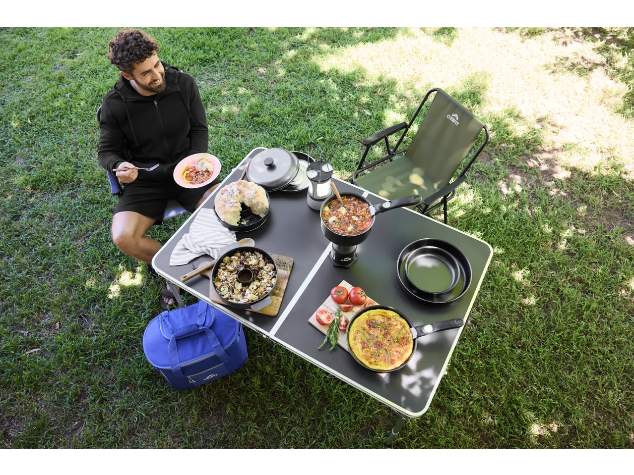 Homem a desfrutar de uma refeição ao ar livre, mesa com comida e cadeira de campismo Crivit.