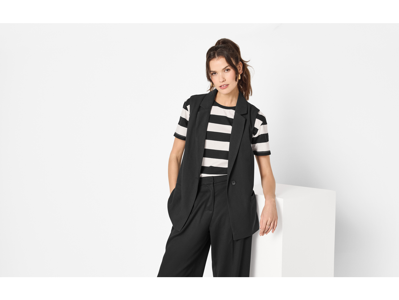 Žena u Esmara sakou bez rukava, prugastoj majici i crnim hlačama.