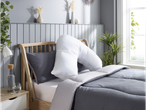 A U-shaped pregnancy pillow rests on a gray duvet-covered bed with gray and white bedding.