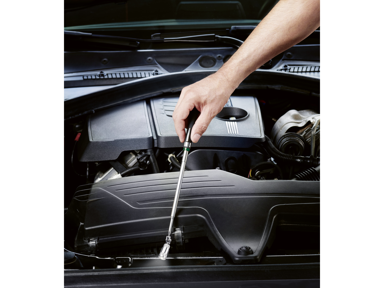 A hand uses a Parkside® magnetic pickup tool to retrieve an object from a car engine.
