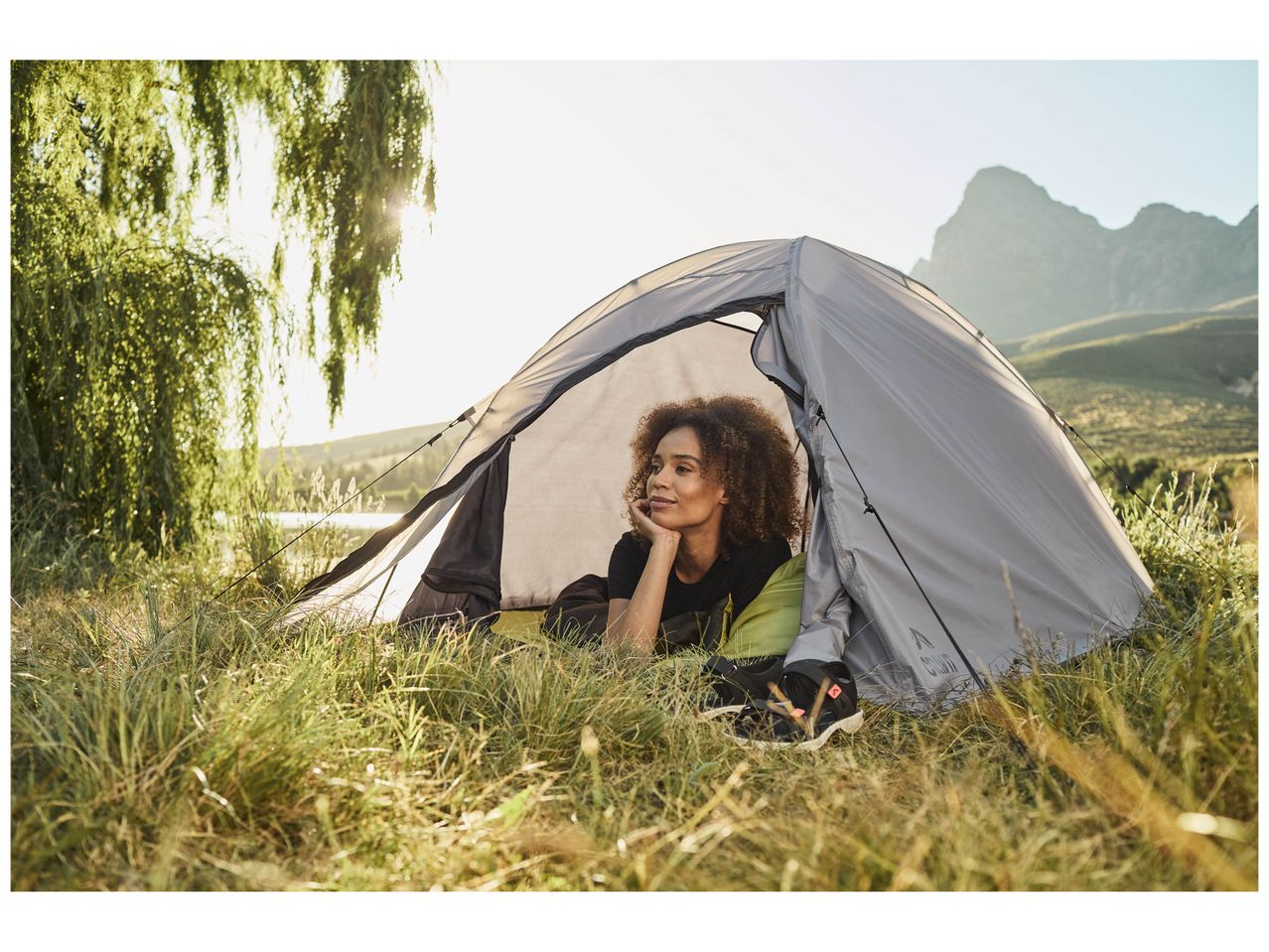 Une femme se repose dans une tente de camping Quechua, près d'un lac et de montagnes.