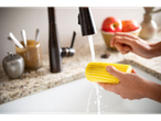 Een hand knijpt een Scrub Daddy spons uit onder stromend water.