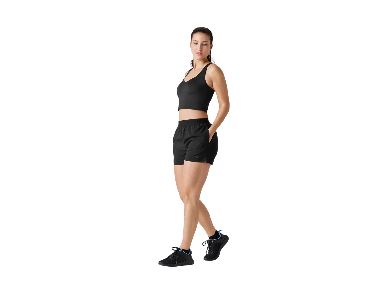 Femeie în sutien sport, pantaloni scurți și adidași negri.