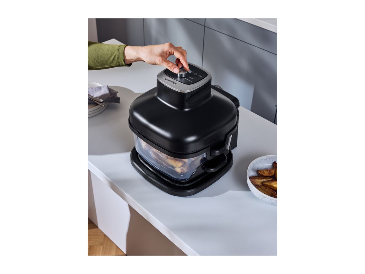 A person's hand adjusting the settings on a black air fryer with potato wedges inside.