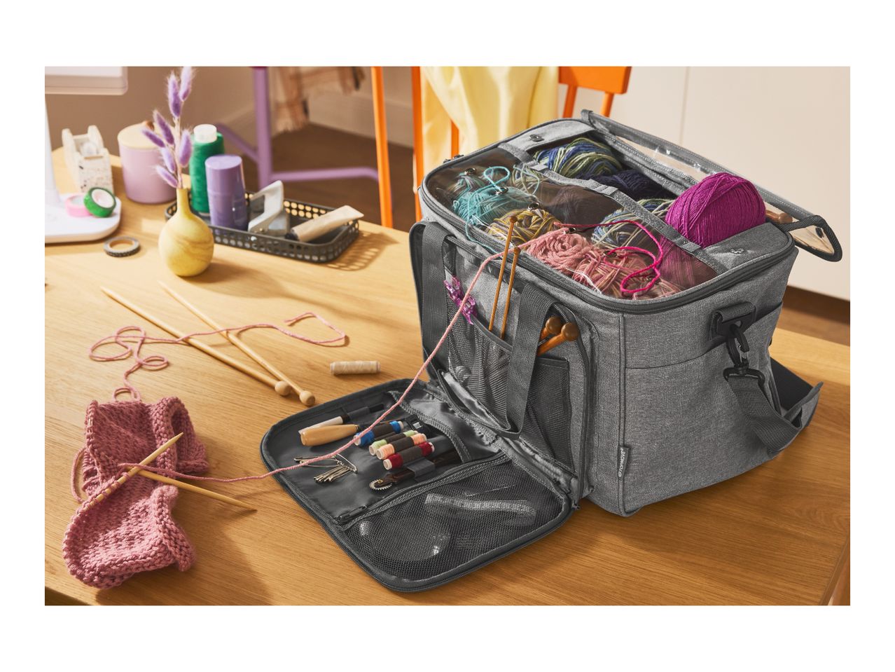 A grey knitting bag filled with yarn and knitting supplies on a wooden table.