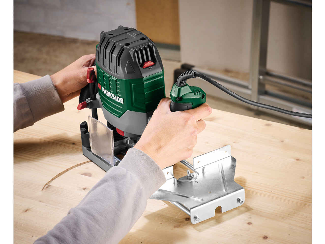 A person using a Parkside® 1200W Router to cut a curved groove in a wooden surface.