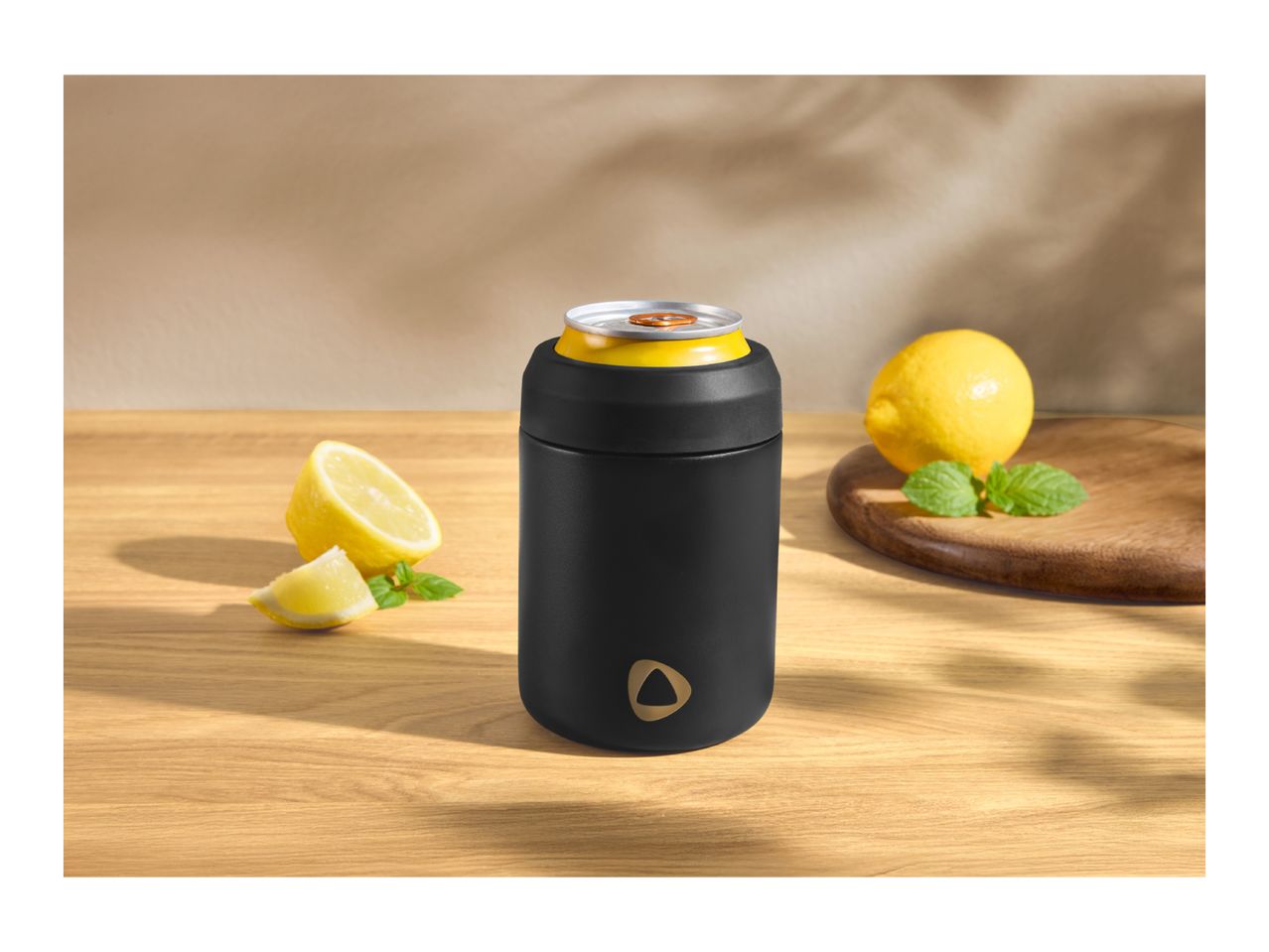 Black can cooler with a yellow drink can, lemons, and mint on a wooden table.