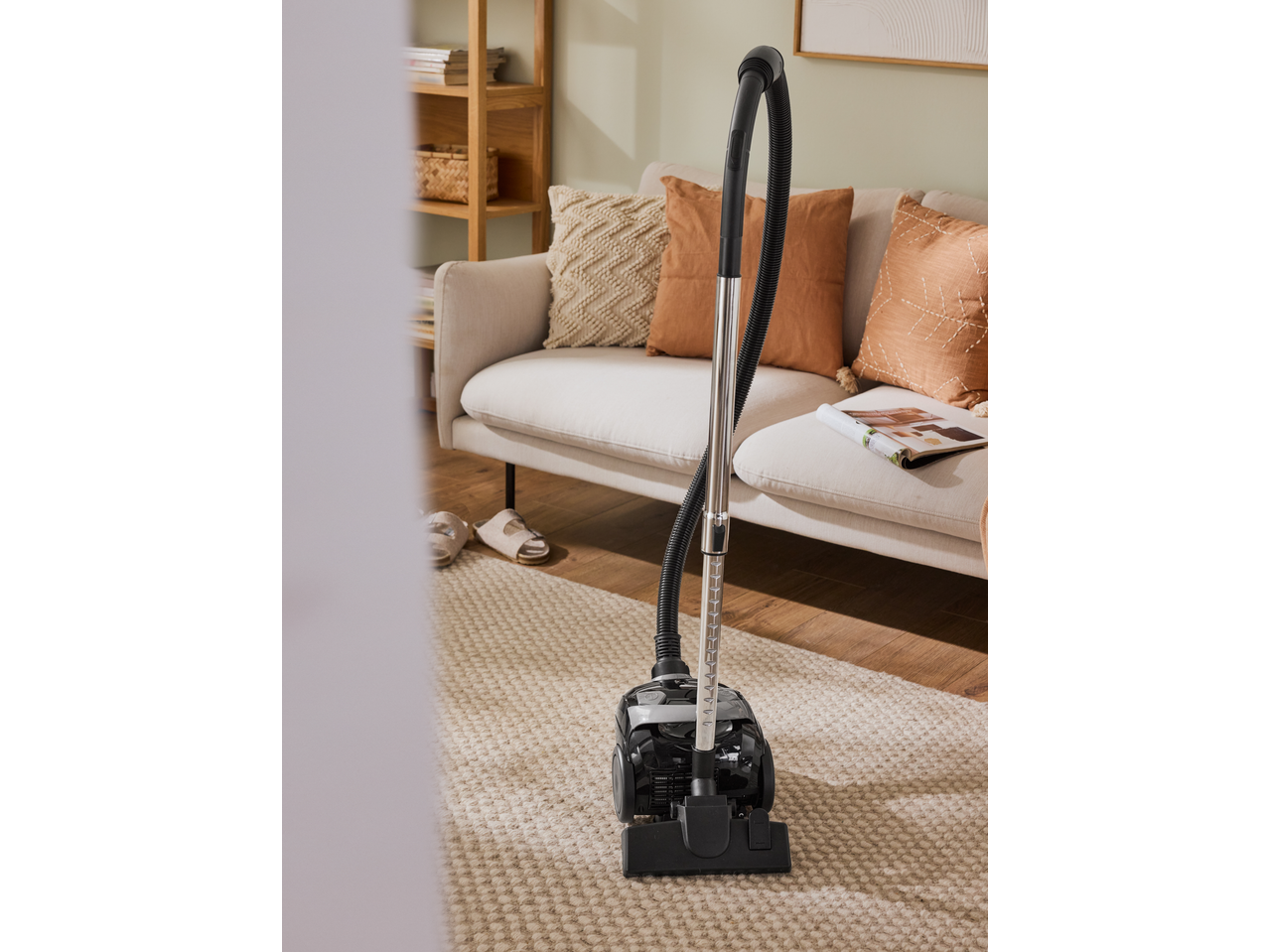 Vacuum cleaner on a textured rug in a living room with a sofa and wooden shelf.