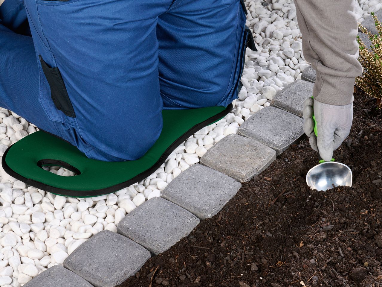 Persona che installa un bordo di pavimentazione in un giardino con una paletta e un inginocchiatoio.