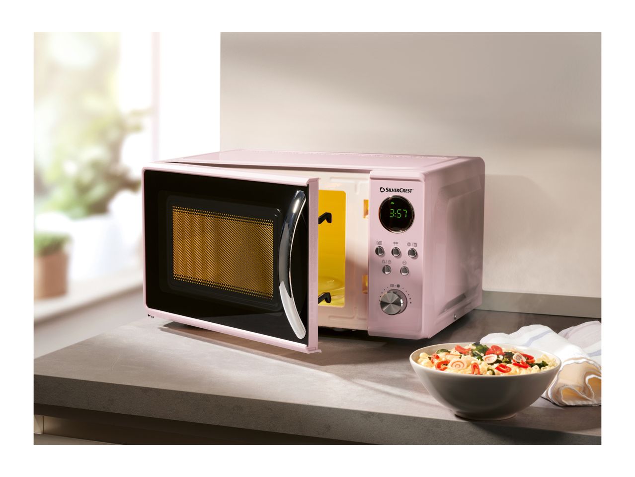 Pink SilverCrest microwave oven with an open door and a bowl of food on the counter.