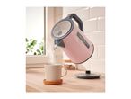 Pink SilverCrest electric kettle pouring hot water into a mug on a wooden counter.