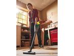 A woman cleans up sawdust in her workshop using a Parkside handheld vacuum cleaner.