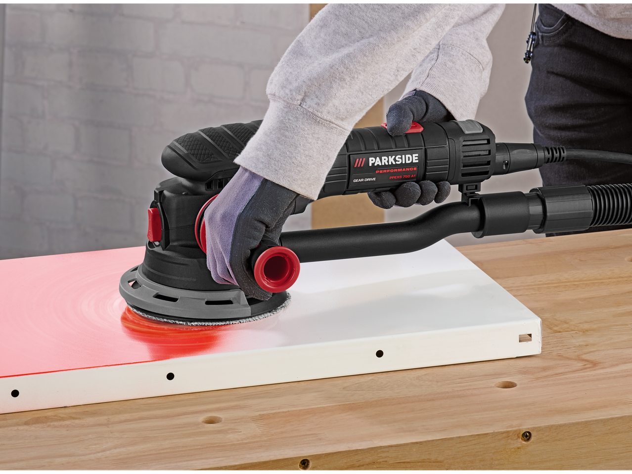 O persoană șlefuiește o suprafață roșie cu un șlefuitor excentric Parkside Performance.