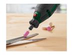Rotary tool with a pink grinding stone sharpening scissors on a wooden surface, with other attachments nearby.