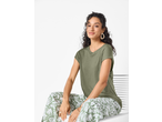 Mulher com t-shirt verde-oliva e calças com estampado floral branco, sentada e sorrindo.