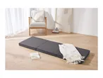 A gray folding mattress on a light wood floor with a white throw blanket and a book.
