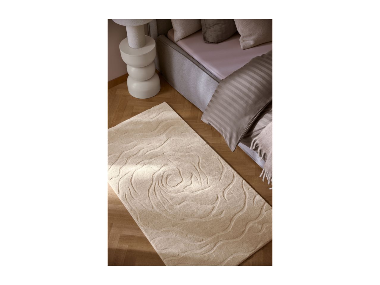 A soft, beige patterned rug on a wooden floor next to a bed.