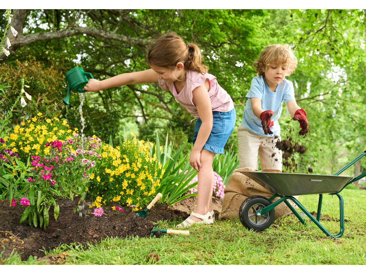 Dvoje djece vrtlare s kolicima i alatom, zalijevaju cvijeće i premještaju zemlju.