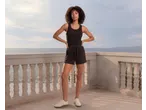 Mulher de top preto e calções numa varanda com vista para o mar.