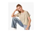 Woman in a beige eyelet t-shirt and wide-leg jeans, posing with her hand on her head.