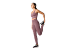 Mulher em roupa desportiva roxa alongando a perna.
