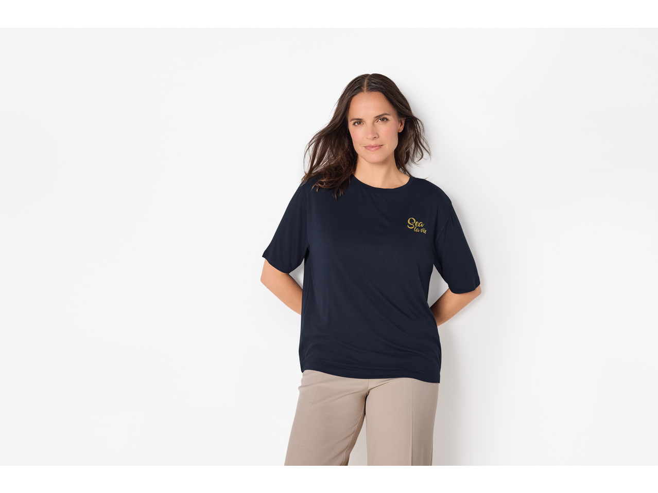 Femeie în tricou albastru cu textul „Sea la vie” și pantaloni bej.