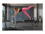 Woman in pink leggings and black sports bra doing pilates on a reformer machine.