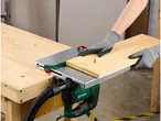 Una persona che indossa guanti di sicurezza taglia un pezzo di legno con un seghetto alternativo montato su un banco da lavoro.