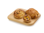 Pastel de nata, pain au chocolat et escargot aux raisins sur une planche en bois.