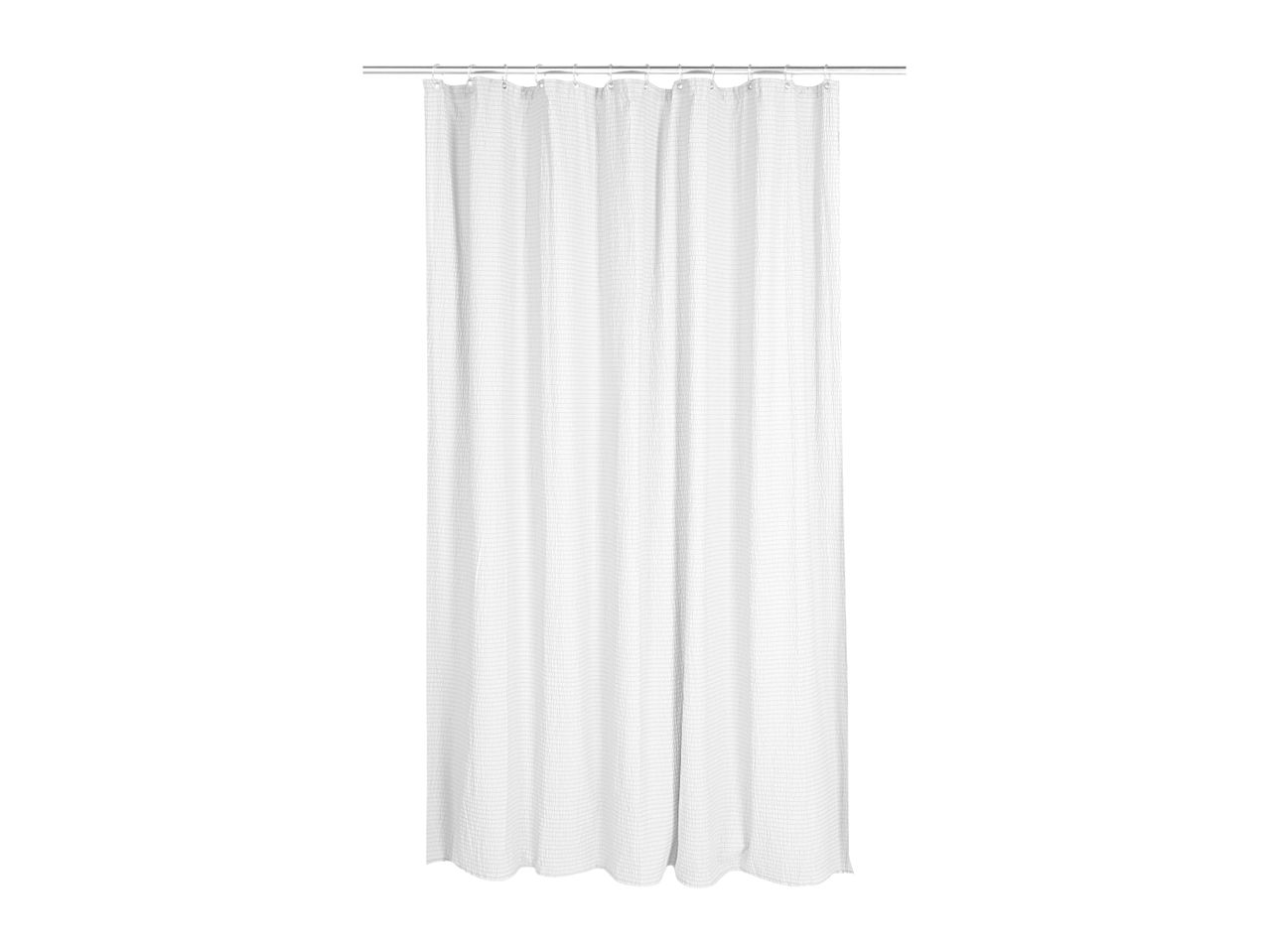 White waffle weave shower curtain hanging from a silver rod with rings