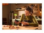 A woman in a workshop uses a screwdriver to work on an electrical component, with other screwdrivers on the wooden table.