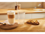 Um copo de café com leite e um copo vazio em uma mesa de madeira, com biscoitos ao lado.