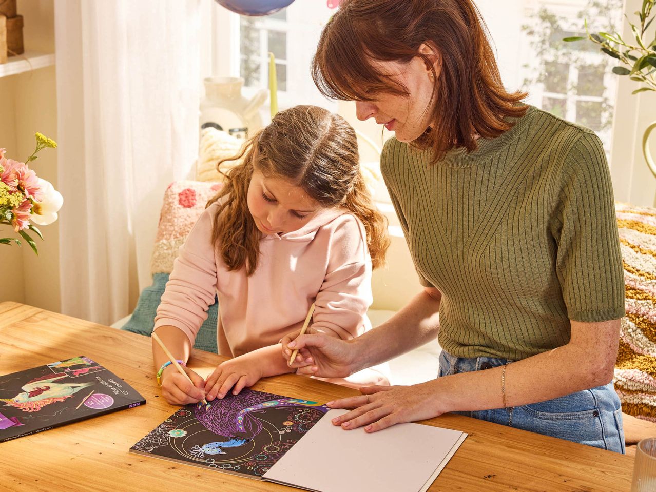 Una donna e una bambina disegnano su libri da grattare con un unicorno e un pavone.