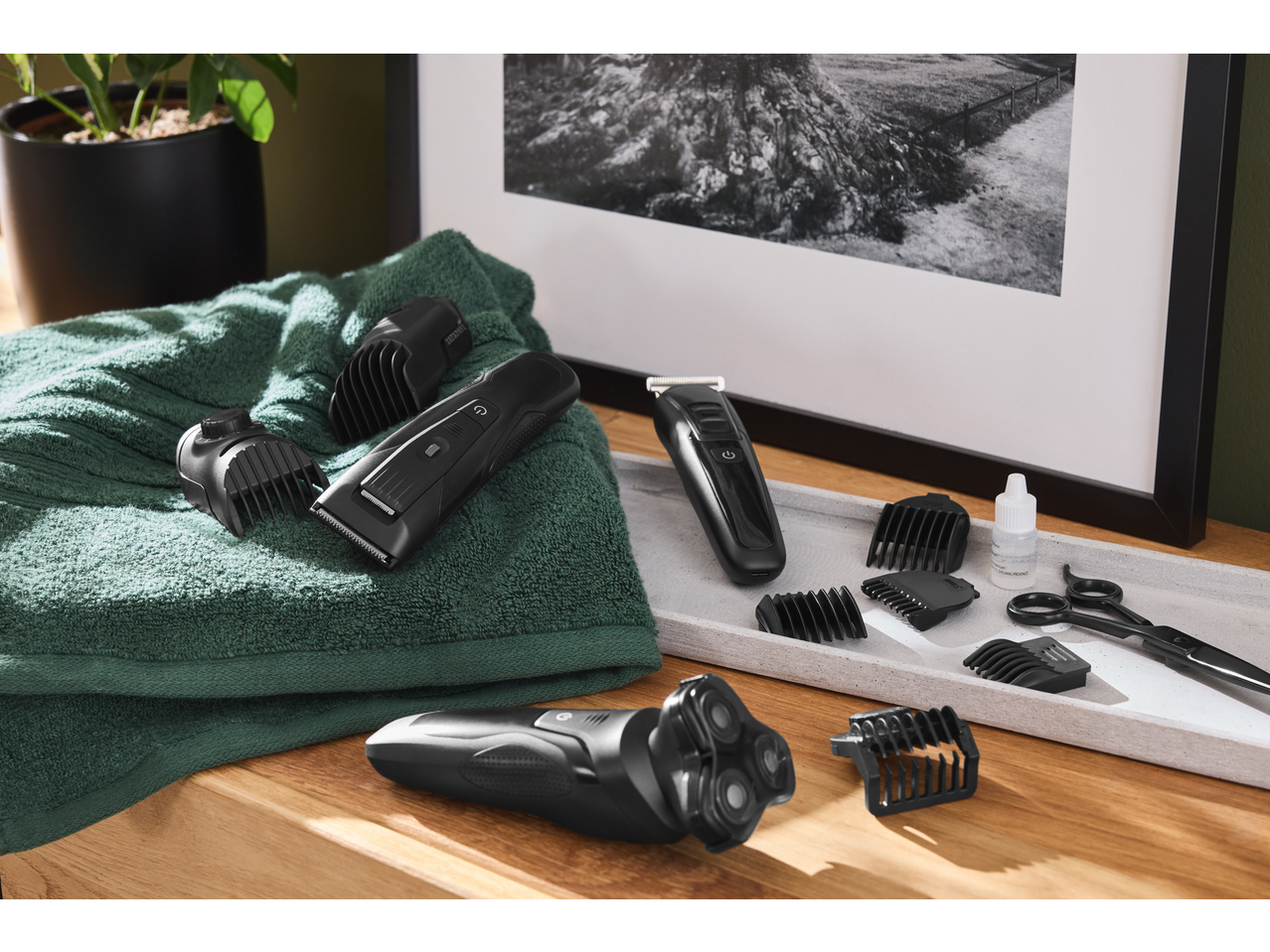 Electric shaver and hair clippers with various attachments, oil, and scissors on a wooden surface.