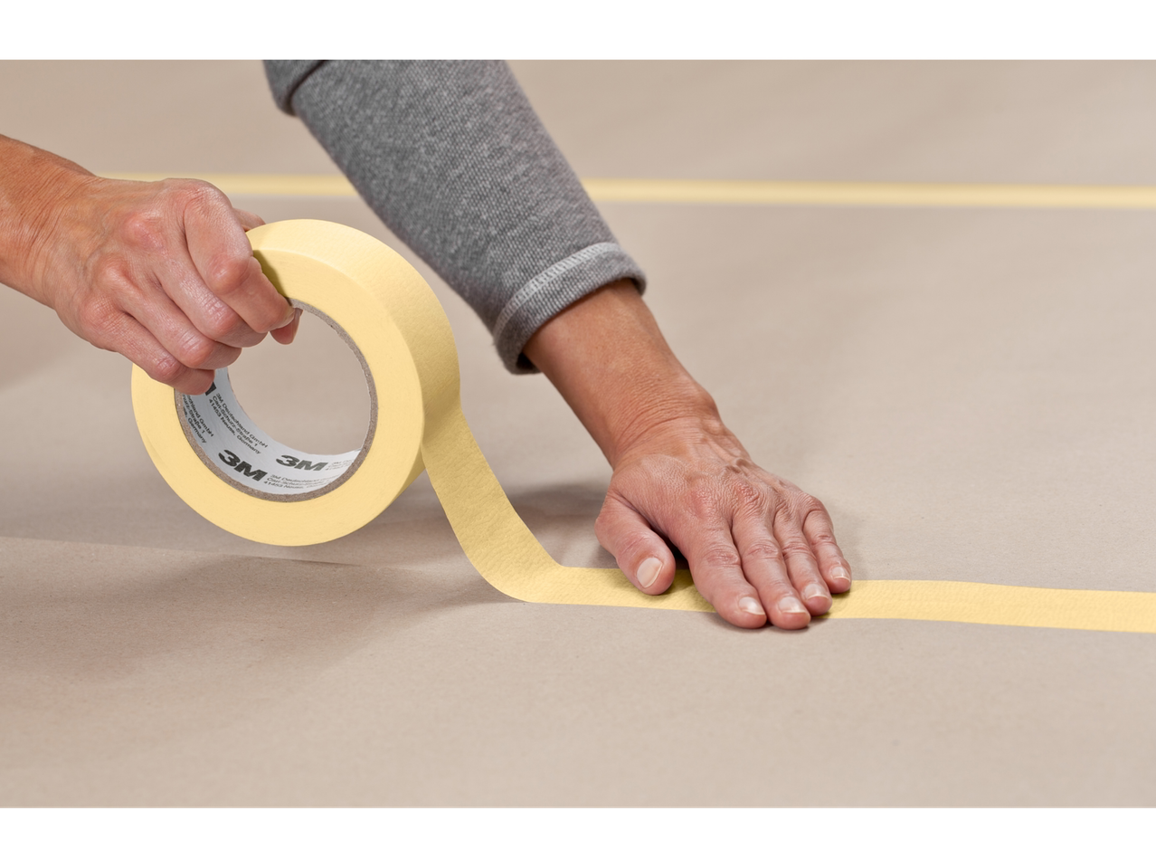 A person applying 3M masking tape to a surface.
