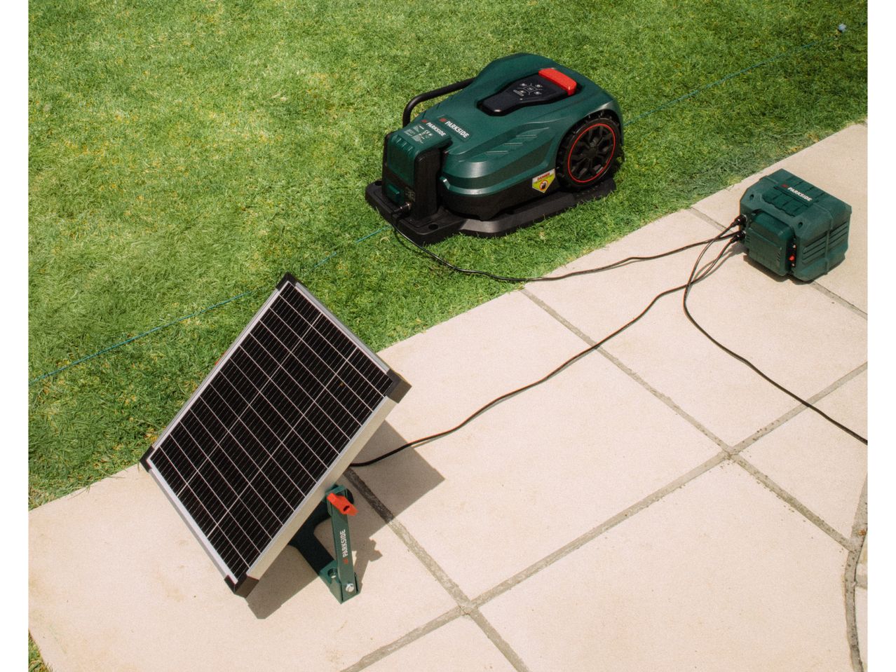 Robotic lawnmower and solar panel charging station on a patio next to grass.