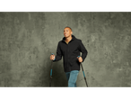 Man in a black CRIVIT Men's Thermal Softshell Jacket and blue pants, holding trekking poles.