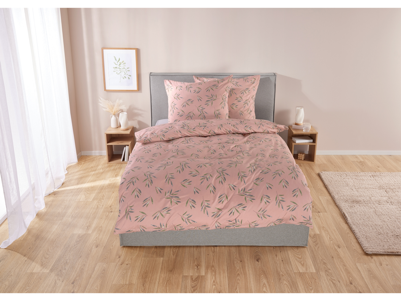 Roze beddengoed met groen bladpatroon op een tweepersoonsbed met houten nachtkastjes.