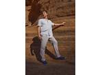 Man in striped short-sleeve shirt, light trousers, and blue espadrilles against a rock wall.