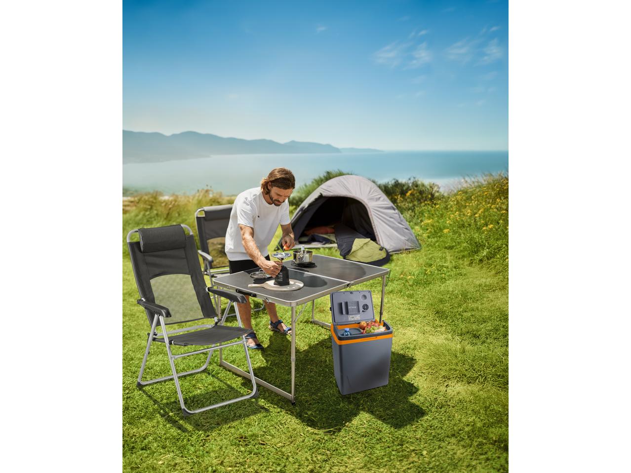 Mann kocht an einem CRIVIT Campingtisch mit Zelt und Meerblick.
