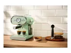 Mint green espresso machine making coffee, with cookies and coffee beans on a wooden counter.