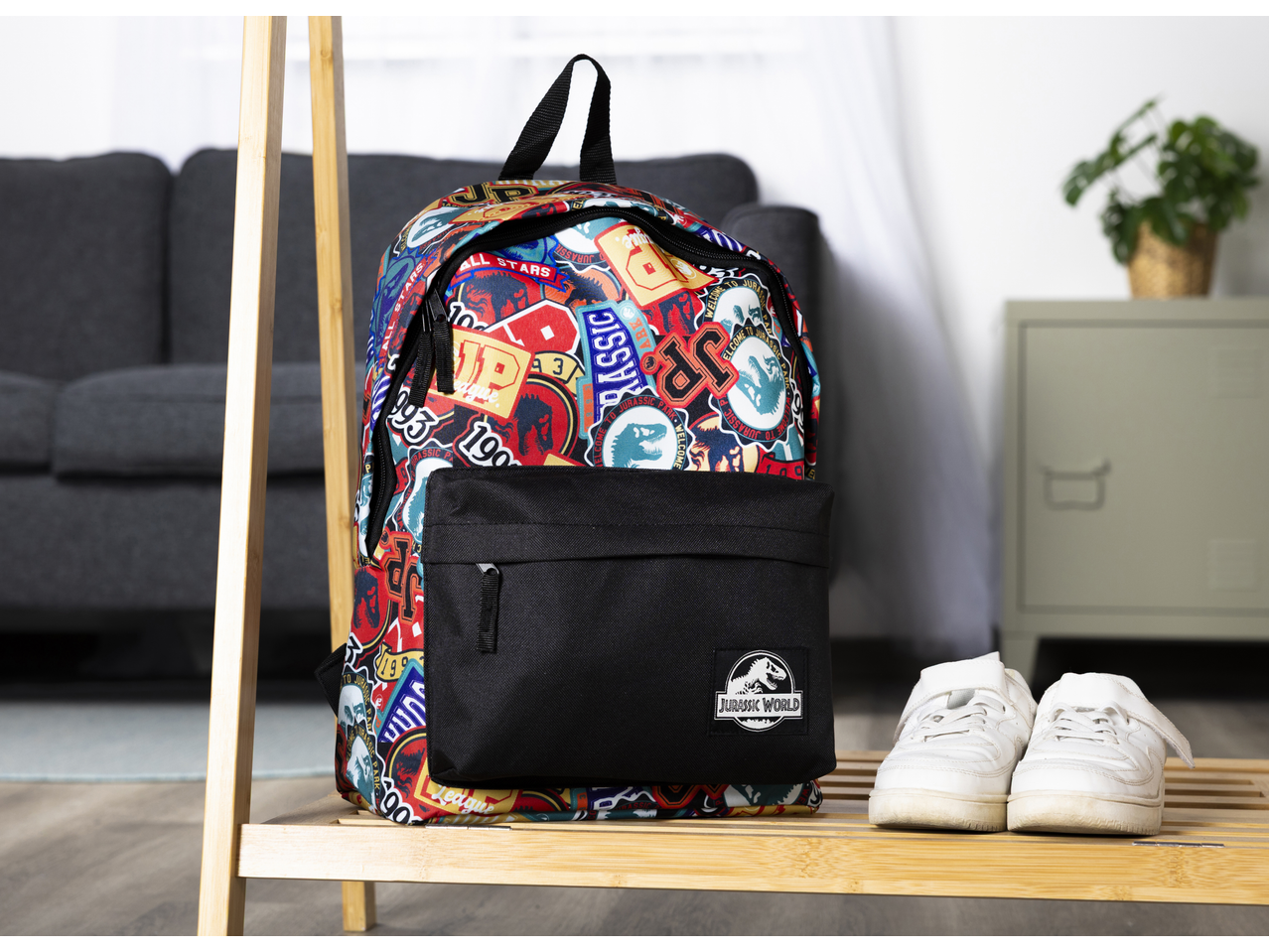 School backpack with Jurassic World print and a pair of white sneakers on a wooden shelf.