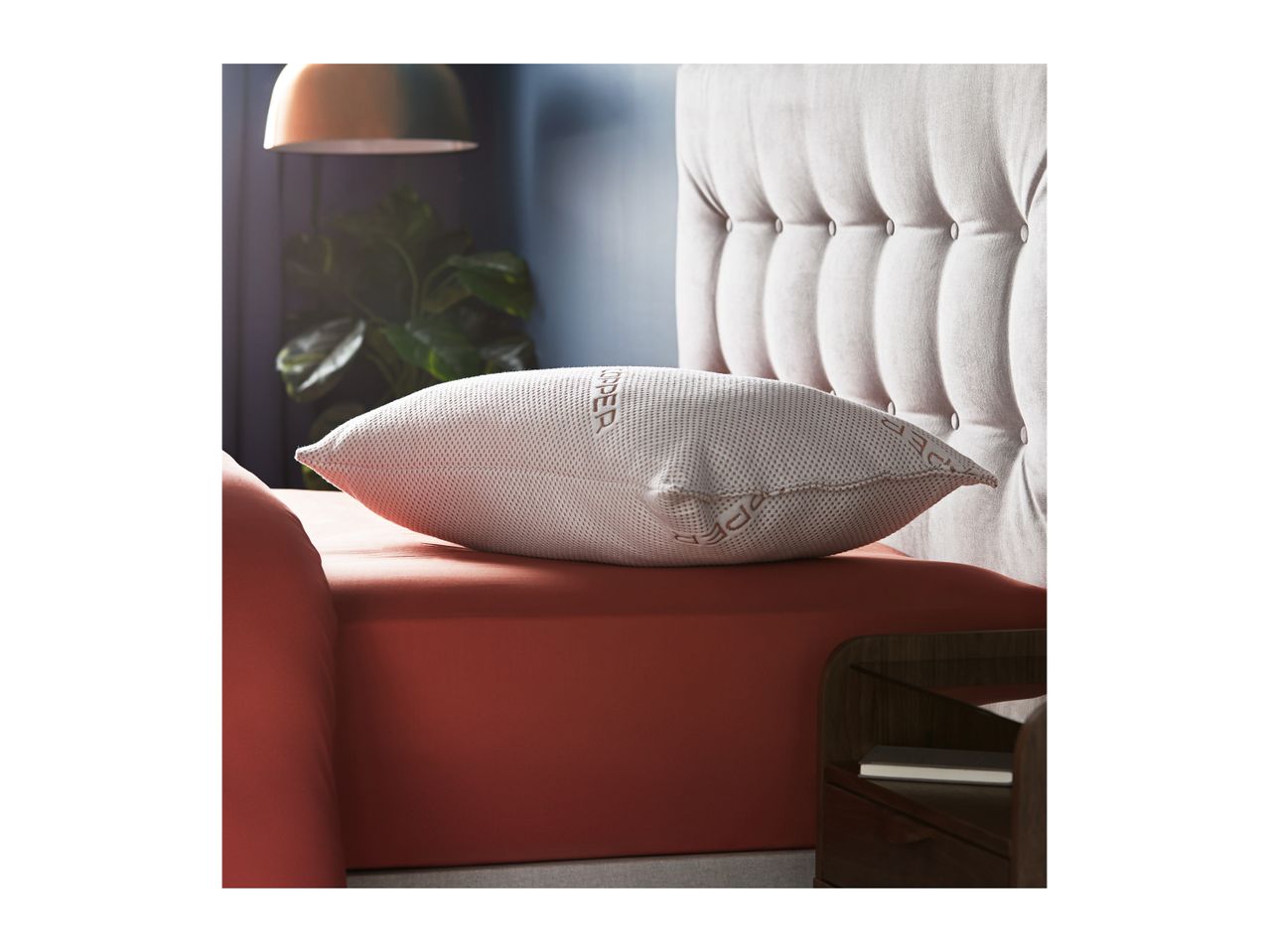 A white pillow with the word 'COPPER' on it rests on a red bed with a tufted headboard.